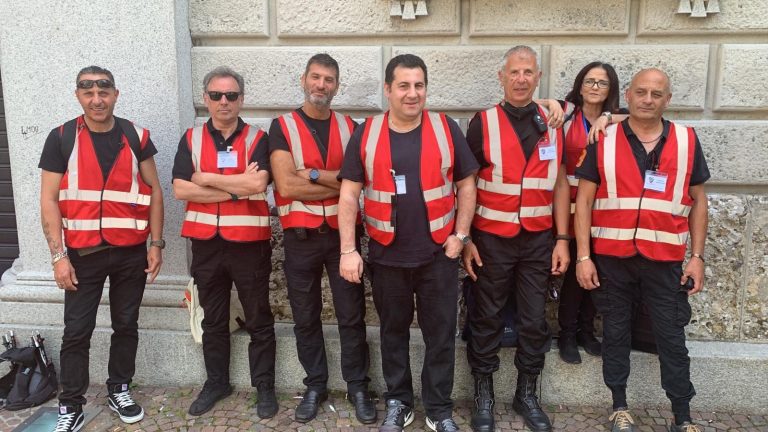 Sei addetti con gilet rosso di riconoscimento davanti all'ingresso di un evento